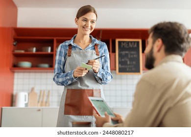 Beautiful friendly waitress taking an order from male customer and writing it down on her notepad, looking at guy and smiling - Powered by Shutterstock