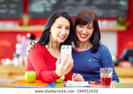 beautiful friends taking a self portrait with phone in cafe