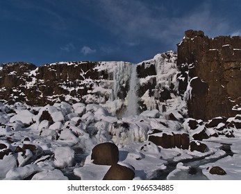 Beautiful front view of Öxarárfoss waterfall in rocky Almannagjá canyon in Þingvellir national park, Golden Circle, Iceland, in winter season with snow and icicles on sunny day.
