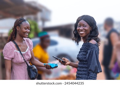 a beautiful fruit vendor, is shown holding a POS terminal, while the other woman, a customer at the market, is using a mobile phone to make a digital payment - Powered by Shutterstock