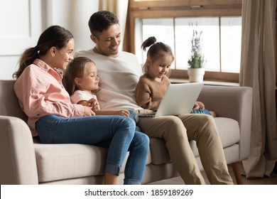 Beautiful Full Family With Two Cute Daughters Resting With Laptop Seated On Sofa. Couple Develop Offspring Watching Educational Online Tv, Buy Goods On Internet, Have Fun Use Modern Technology Concept