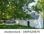 Beautiful full frame image of a colonial whitewashed stone springhouse surrounded by natural green grass and lush summer foliage.