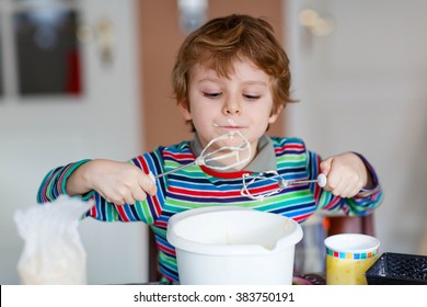 Beautiful Funny Blond Little Kid Boy Baking Cake And Tasting Dough In Domestic Kitchen. Happy Child Having Fun With Working With Mixer, Flour, Eggs And Fruits At Home.