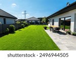 Beautiful garden with green grass, visible terrace table and house in beautiful summer weather, very wide shot.