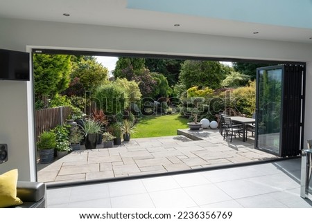 Beautiful garden and patio in summer seen from stylish designer room through bifold doors.
