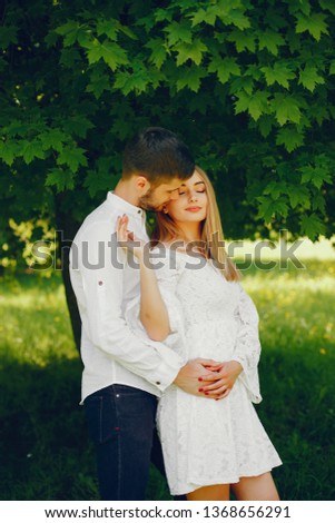 A beautiful and gentle girl with light hair and a white dress is walking in a sunny summer forest with her handsome guy in a white shirt and dark pants