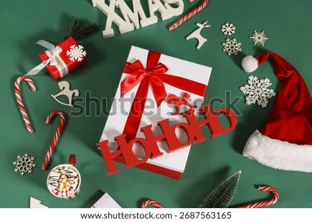 Beautiful gift boxes with candy canes, Christmas decorations, cup of cacao and word HOHOHO on green background, top view