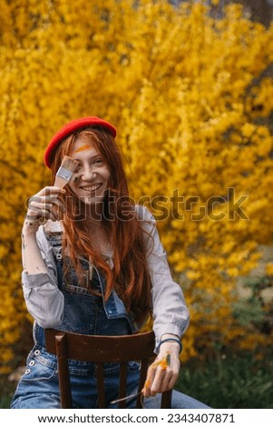 Beautiful giger girl posing with her big brush on her eye and smiling while sitting in front of the yellow flowers