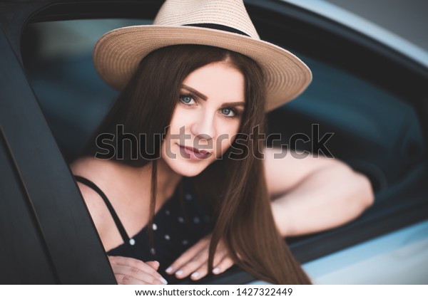 Beautiful girl 20-24 year old\
wearing straw hat sitting in car. Looking at camera. Summer time.\
