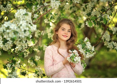 Beautiful girl 9 years old in flowering Apple trees. Long blonde hair, blue eyes, curls.