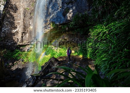 A beautiful girl admires rainbow while a walk behind a spectacular tall waterfall while hiking the Warrie Circuit trail in Springbrook National Park, Gold Coast, Queensland, Australia	