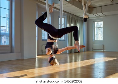 Beautiful girl aerial yoga trainer shows medutiruet on hanging lines upside down in a yoga room. Concept yoga, flexible body, healthy lifestyle, fitness.
