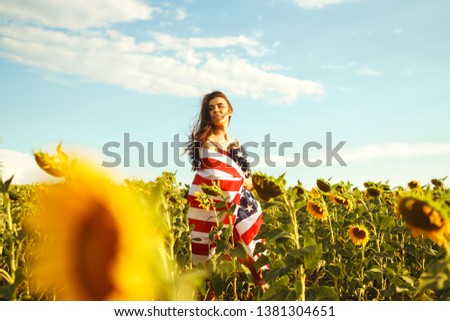 Beautiful girl with the American flag in a sunflower field. 4th of July. Fourth of July. Freedom. Sunset light The girl smiles. Beautiful sunset. Independence Day. Patriotic holiday.