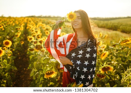 Beautiful girl with the American flag in a sunflower field. 4th of July. Fourth of July. Freedom. Sunset light The girl smiles. Beautiful sunset. Independence Day. Patriotic holiday.