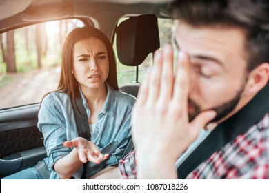 Beautiful girl is arguing with her boyfriend. She is not satisfied. Guy is covering his face with hand. He is very tired of that. They are sitting in car.