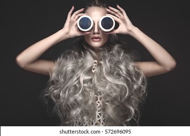 Beautiful girl in art dress and avant-garde hairstyles with cosmetic products in her hands. Beauty face. Photos shot in the studio. - Shutterstock ID 572696095