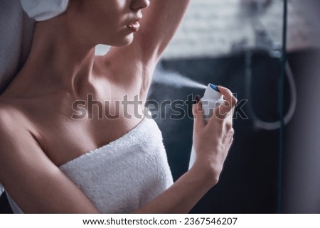 Beautiful girl in bath towel is applying deodorant while standing in bathroom after having a shower