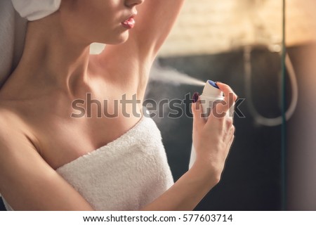 Beautiful girl in bath towel is applying deodorant while standing in bathroom after having a shower