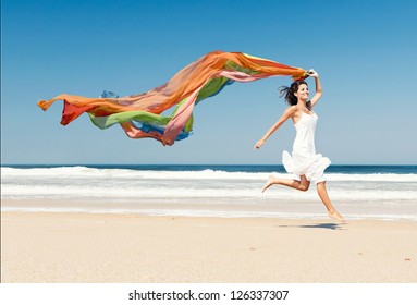 Beautiful girl in the beach running and holding a colored piece of fabric - Powered by Shutterstock