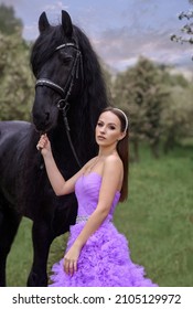 Beautiful girl with a black Friesian horse in spring in a blooming garden in spring. Bride with horse