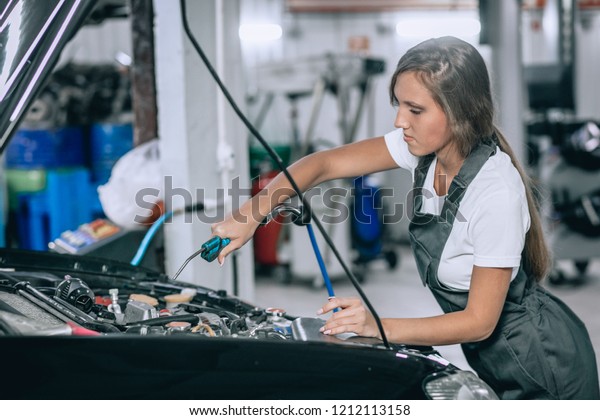 Beautiful girl in\
a black jumpsuit and white t-shirt in overalls examining under hood\
of car in the repair\
garage
