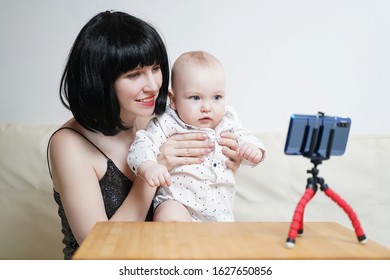 A Beautiful Girl Blogger With A Child Leads A Live Broadcast. Mommy Blogger With A Baby Records A Video For A Blog On A Smartphone