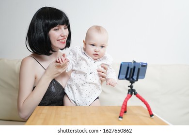 A Beautiful Girl Blogger With A Child Leads A Live Broadcast. Mommy Blogger With A Baby Records A Video For A Blog On A Smartphone