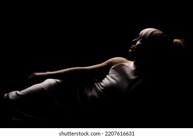 Beautiful Girl With Blond Bangs Fringe Wearing White Fashionable Fancy Dress Lying Against Black Background.