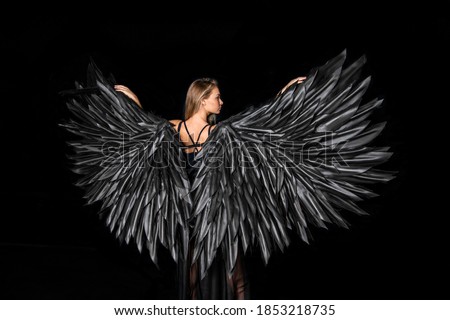 beautiful girl with blond hair in a suit with black angel wings on a black background