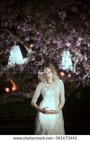Beautiful girl in blooming cherry garden at night. Sadness and melancholy concept. Springtime sadness