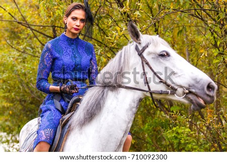 beautiful girl in a blue dress riding a white horse