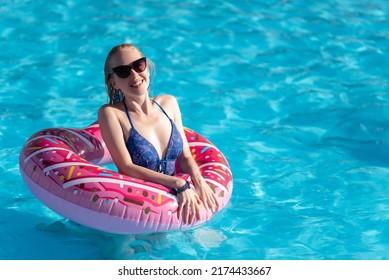Beautiful girl in a blue swimsuit, sunglasses swims in a pink inflatable circle in the shape of a donut