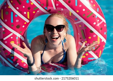 Beautiful girl in a blue swimsuit, sunglasses floats in a pink inflatable circle in the shape of a donut. Laughing and throwing up his hands