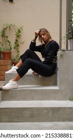 A Beautiful Girl With Boho Style Dreadlocks Is Sitting On The Steps. Hippie Woman Posing In Black Bohemian Outfit. Street Style. Girl With Tattoos In A Cafe