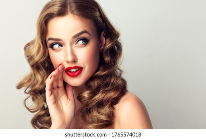Beautiful girl with bright makeup and curly hair   telling a secret .Portrait  young happy woman who is calling to someone .Funny girl model  whispering about something. Expressive facial expressions

