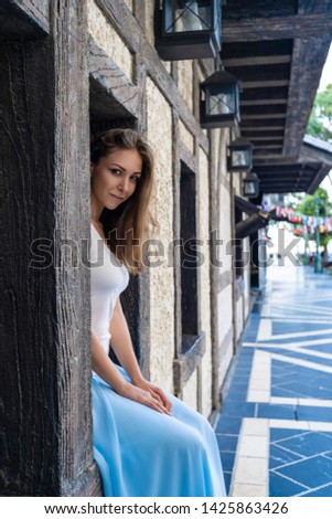 Beautiful girl with brown hair is sitting in the window of stone-wooden wall in building in dutch style in Europe