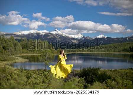 beautiful girl, brunette in a yellow dress walks near a mountain lake