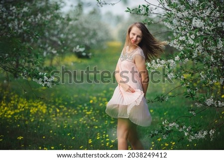 Beautiful girl in a cherry blossom garden. Woman in a pink dress and a field of yellow dandelions. Blooming cherry orchard and charming girl in a dress. Beautiful warm spring