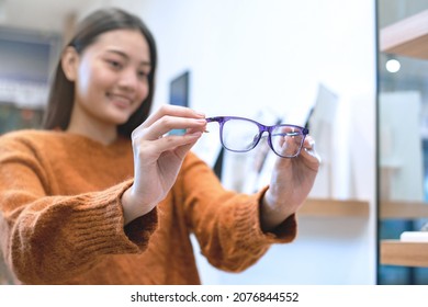 Beautiful Girl Choosing A Glasses In Optician Store, Asian Girl In Sweater With Different Models Of Glasses, Selective Focus