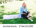 beautiful girl city park blue blazer white blouse black pants hat wind hair model summer sitting on pad grass with tablet reads documents folder instruce guide