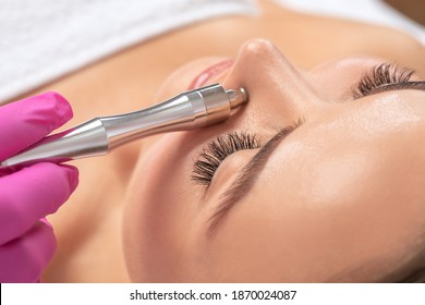 Beautiful girl with clean fresh skin.Cosmetologist makes  procedure microdermabrasion on the face against acne and blackheads on the nose. Women's cosmetology in the beauty salon.