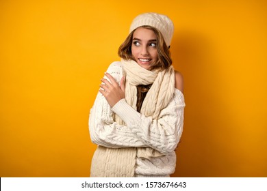 Beautiful Girl With Clean Skin And Loose Curls In A White Sweater And Hat On A Yellow Background, Wrapping Herself In A Scarf