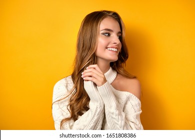 A Beautiful Girl With Clean Skin And Loose Curls In A White Sweater Stands Smiling And Looks To The Side On A Yellow Background