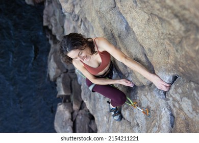 Beautiful Girl Climbs A Rock Above The Water. Sport Climbing In Nature. Extreme Sport. Fitness And Beauty