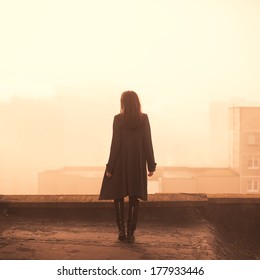 beautiful girl in a coat on a rooftop in the city. morning photo
