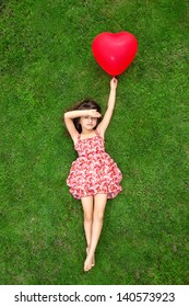 beautiful girl in color dress lying on the grass and holding a red ball in the form of heart