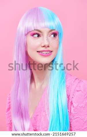 Beautiful girl with colored purple-blue hair and bright pink makeup with shiny glitter freckles. Studio portrait on a pink background. Hairstyle, hair coloring. Make-up and cosmetics.