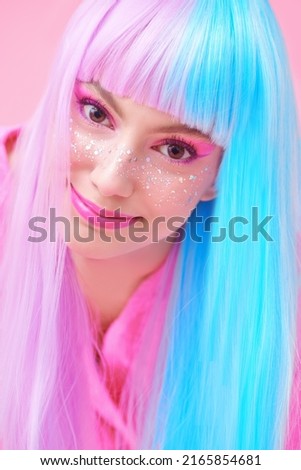 Beautiful girl with colored purple-blue hair and bright pink makeup with shiny glitter freckles. Studio portrait on a pink background. Hairstyle, hair coloring. Make-up and cosmetics.