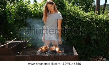 Beautiful girl cooking hen n the sticks outdoors in green bushes