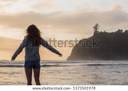 Beautiful girl with curly hair stands looking out at the sea at Olympic National Park in Washington on the coast with arms wide